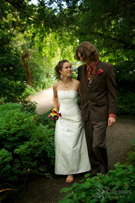 bride and groom walk through wooded path in garden