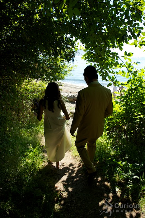 bride and groom walk through tunnel of green down to beach
