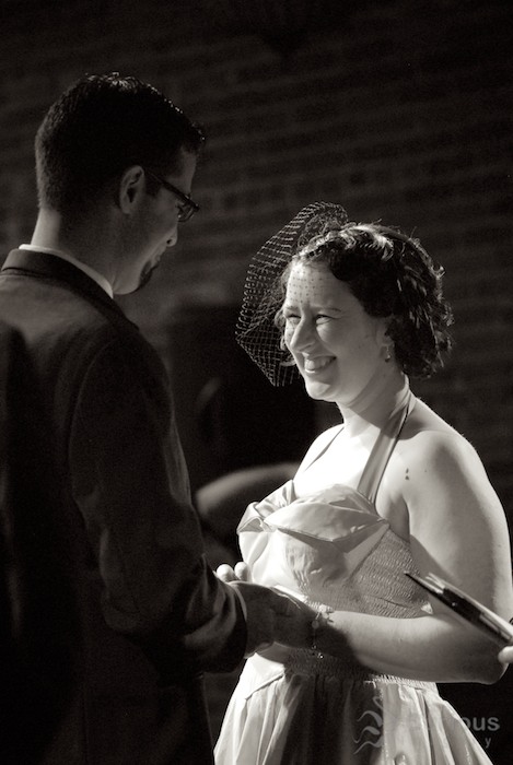 Bride and groom smile at each other during wedding ceremony. Telephoto, black and white.